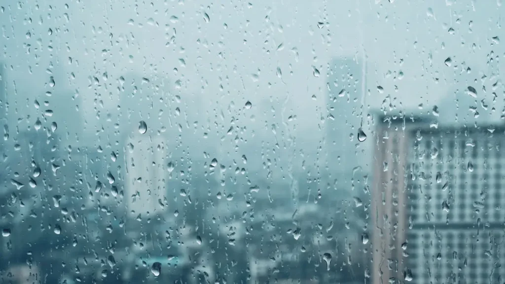 Una ventana con gotas de lluvia y un fondo de ciudad borroso en tonos azules y grises claros