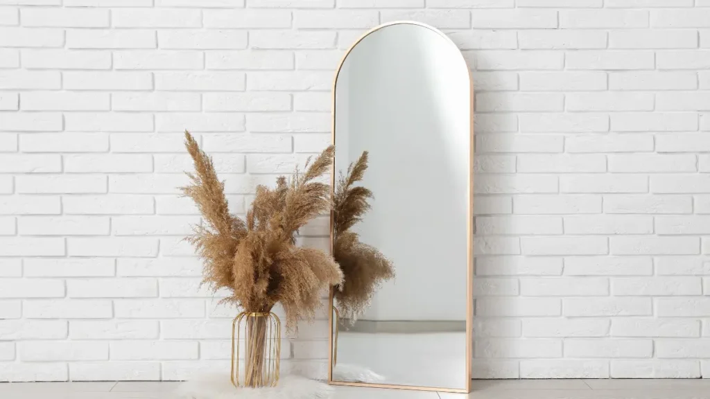Un espejo de arco minimalista al lado de plantas secas sobre un fondo de pared blanca iluminada