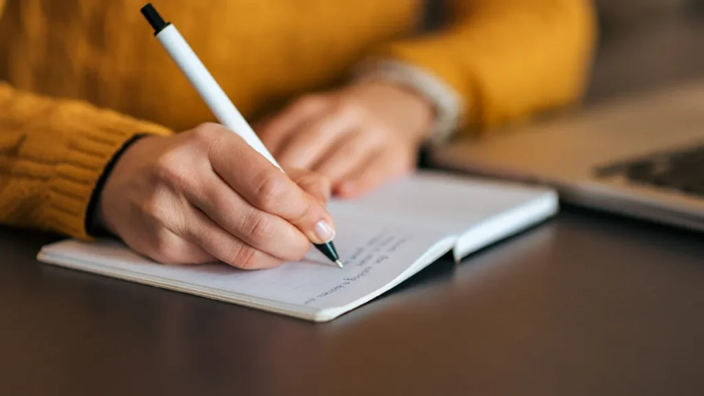 Manos de una persona escribiendo en un cuaderno de notas sobre un escritorio