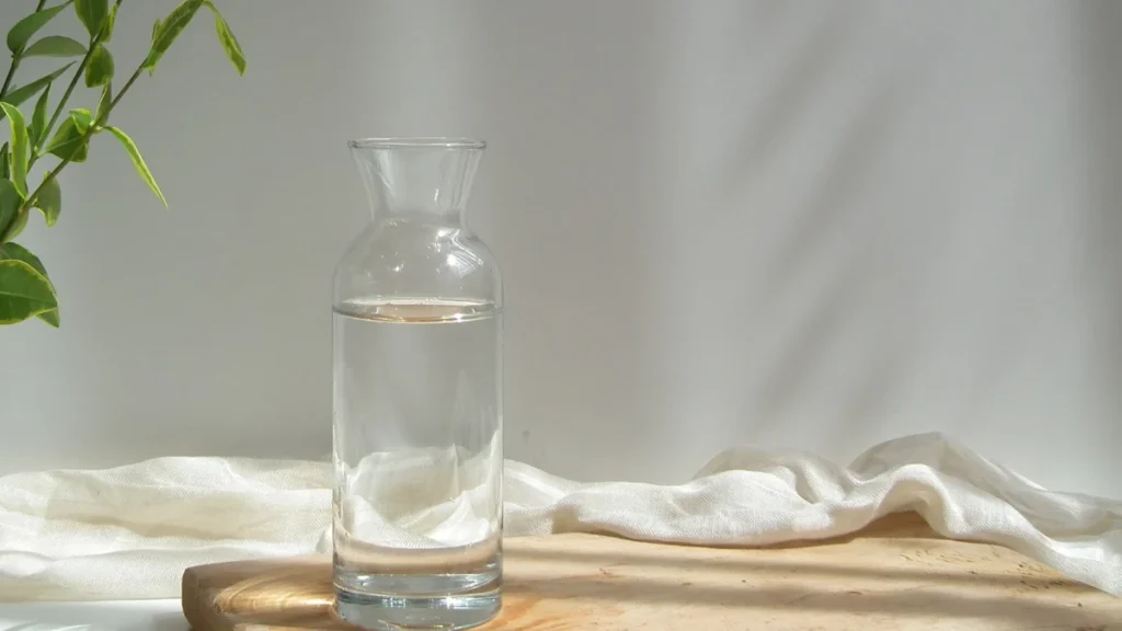 Una botella de vidrio y un vaso de agua sobre una mesa de madera con luz natural suave