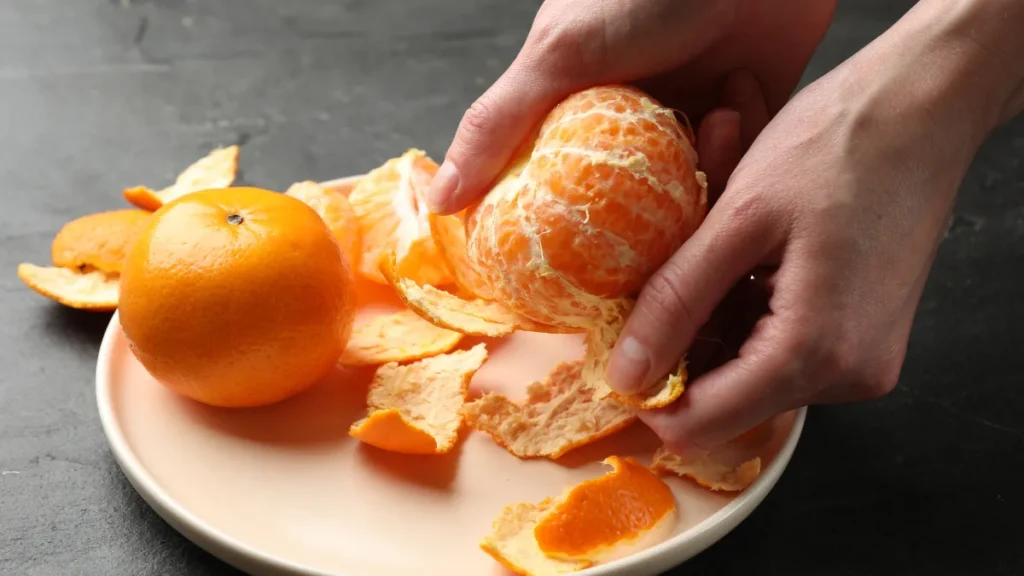 Primer plano de unas manos pelando una mandarina fresca sobre un plato de cerámica con luz suave