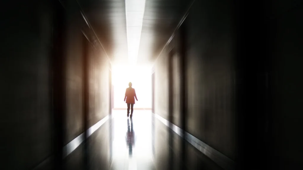 Una persona caminando a través de un túnel oscuro hacia una salida brillante iluminada por luz natural