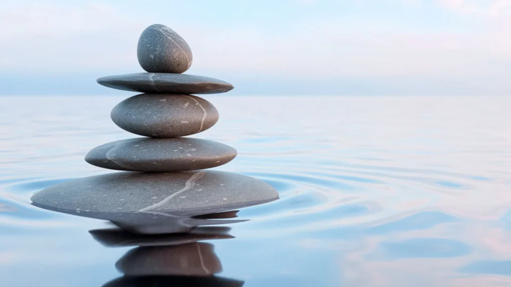 Piedras lisas de río superpuestas en perfecto equilibrio sobre agua tranquila con un fondo claro